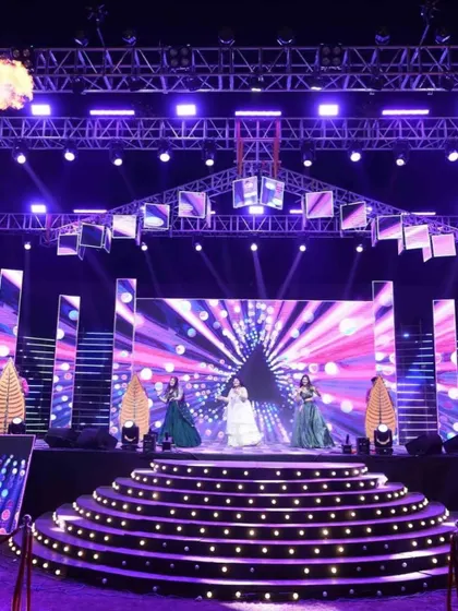 A full view of a spectacular Sangeet stage, complete with multi-level platforms, intricate lighting design, and professional dancers, ready for a night of stunning performances.