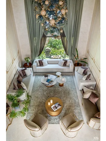 An overhead view of the double-height living room, highlighting the symmetrical furniture arrangement and the grand scale of the space. The large window provides a beautiful view of the garden.