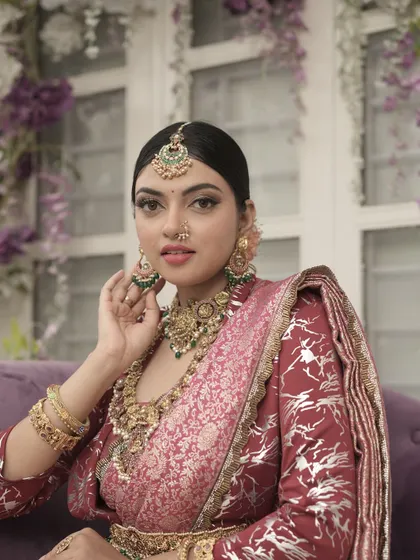 A close-up portrait from the same shoot. The lighting beautifully captures the details of the makeup and the intricate green and gold jewelry.