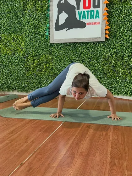 A student smiling as she holds Astavakrasana (Eight-Angle Pose), an arm balance that requires both strength and a sense of play.