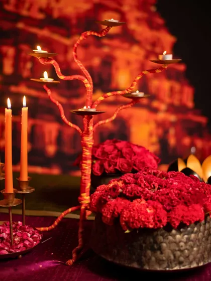 A 'Rang Saari' tablescape for an intimate dinner, featuring a tree-like candelabra wrapped in red thread, bold floral arrangements, and traditional candle holders.
