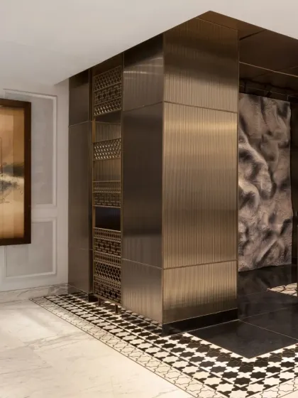 The design uses a deliberate color transition, moving from light marble to dark flooring, to draw visitors toward the reception desk. This visual shift is reinforced by architectural elements like the intricately detailed columns and the sculptural backdrop.