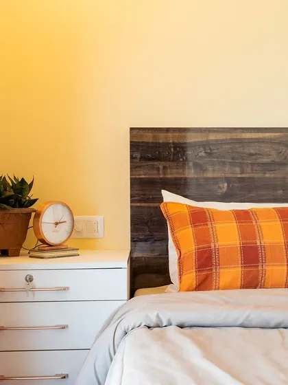 A cozy bedroom with a rustic wood headboard and a pop of color from the plaid pillow.