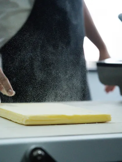 A cloud of flour being dusted over a butter slab for lamination. This shot captures the foundational steps of creating perfect puff pastry.