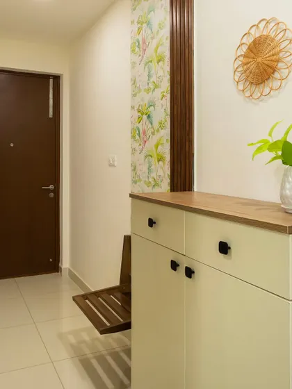 The foyer in 'Bohemian Bliss' features a space-saving shoe cabinet with a foldable seat, set against a backdrop of tropical wallpaper.