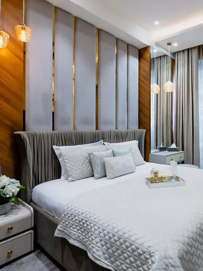 A wider view of the serene grey and gold bedroom, showing the elegant pendant lights and simple, clean-lined bedside tables.