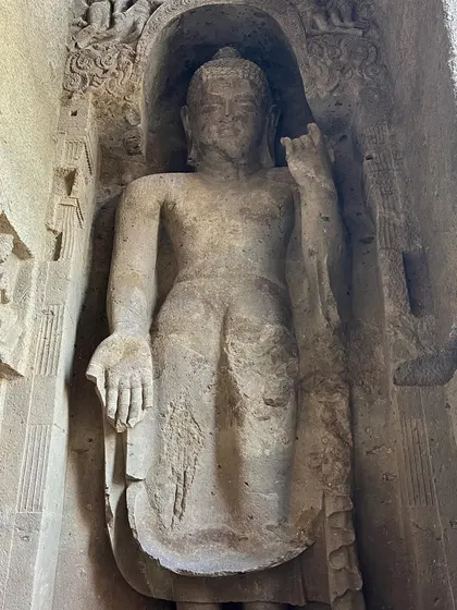 A full-length view of a large standing Buddha statue carved into the rock at Kanheri.