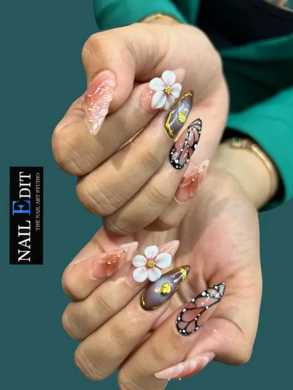 This set demonstrates our mastery of mixed-media nail art on long, stiletto extensions. We've combined delicate, hand-sculpted 3D white flowers, detailed butterfly wing art, and a rich chrome finish with gold accents for a truly statement-making look.