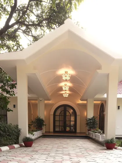 A closer view of the Doon Homestay's entrance portico. The design balances architectural form with soft landscaping, using potted plants and low hedges to soften the lines and guide visitors toward the arched doorway.