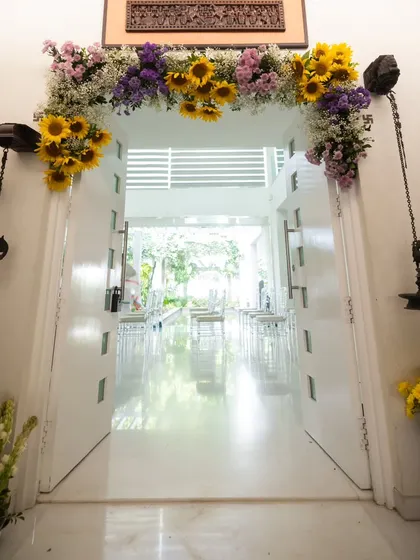 A grand and welcoming entrance for a traditional baby welcome ceremony. The doorway is adorned with a beautiful arch of sunflowers and other fresh blooms, leading into a bright, serene space.