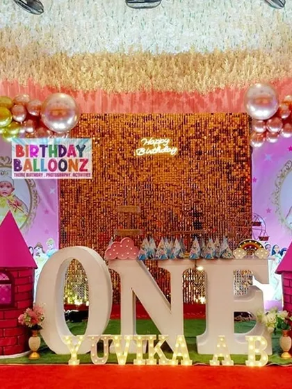 A grand princess castle theme for a first birthday. The stage is decorated with pink castle props, a sparkling gold backdrop, personalized photo frames, and a large "ONE" marquee sign, creating a royal celebration.