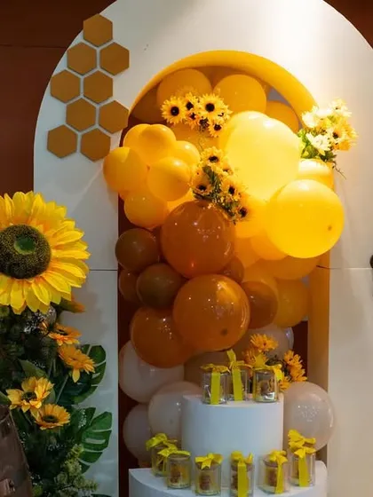 A detail shot from the "Mom to Bee" party, showing the cake and dessert area with a sunflower and balloon-filled arch.