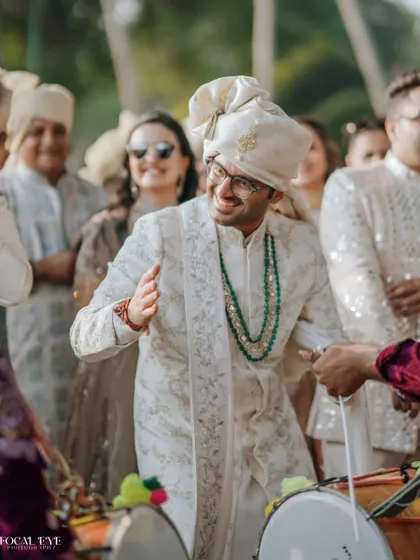 The groom's joy is infectious as he joins the dhol players during his baraat procession, a candid moment full of energy.