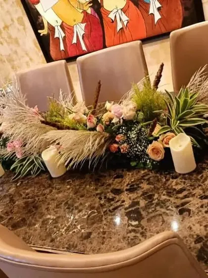 A modern centerpiece for a dinner table, featuring a mix of pink roses, pampas grass, and pillar candles. This style is perfect for creating a warm, rustic, and stylish ambiance.