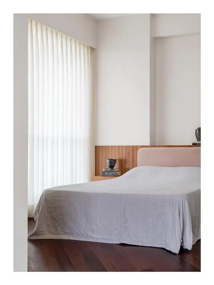 A bedroom designed for restraint and calm. The custom bed features a simple, low headboard in a soft, neutral fabric, set against a dark wood floor to create a space that lets you breathe.