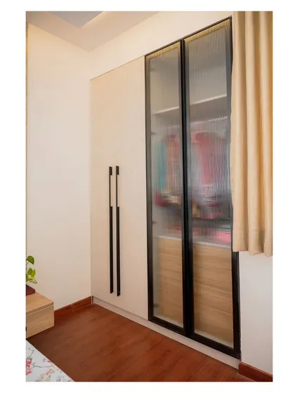 This bedroom features a modern wardrobe with fluted glass doors. The simple, automated curtains next to it ensure that the window treatment is functional without detracting from the room's clean design.