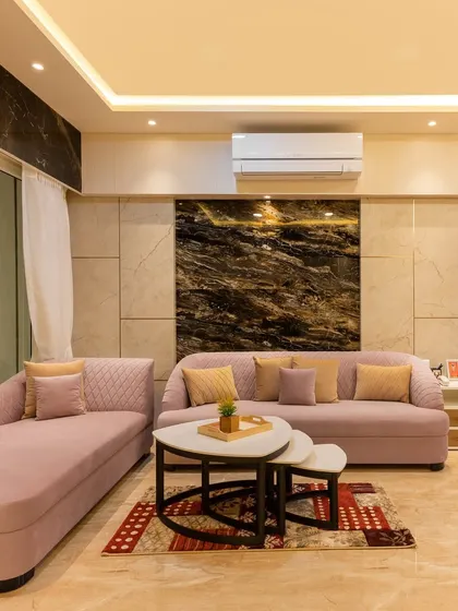 A plush, dusty pink sofa set against a dark marble accent wall creates a sophisticated and comfortable living area.