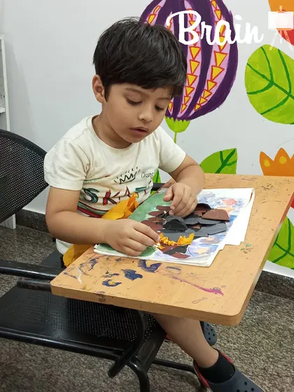This student is fully engaged in his paper collage project, deciding where each piece should go. This kind of creative decision-making helps build confidence and problem-solving skills.