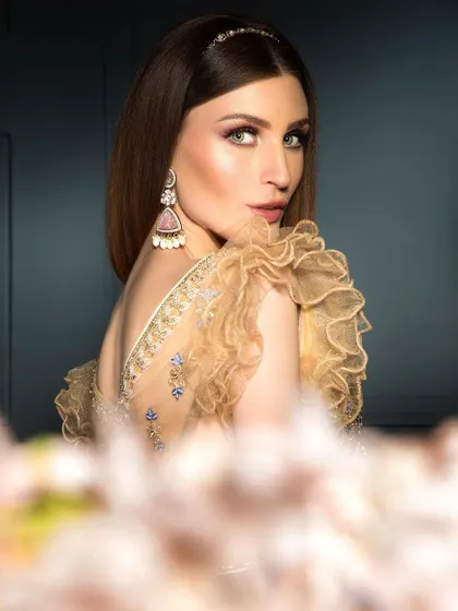 A close-up beauty shot where the model looks over her shoulder. The soft focus on the foreground flowers adds depth, drawing the viewer's eye to the model's expression and the ruffled sleeve details.