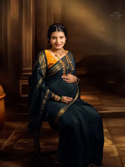 A timeless, painterly portrait of a mom-to-be seated gracefully, looking directly at the camera with a gentle smile.