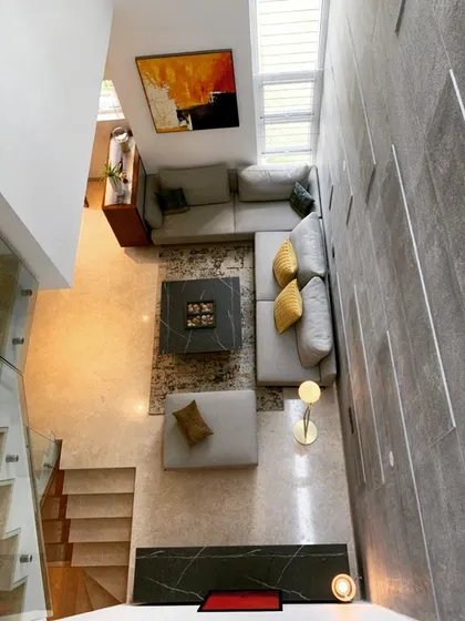 A bird's-eye view of a double-height living room reveals a carefully composed layout with an L-shaped sofa and a prominent stone feature wall. This perspective highlights the spatial planning and the flow between the ground floor and the staircase.