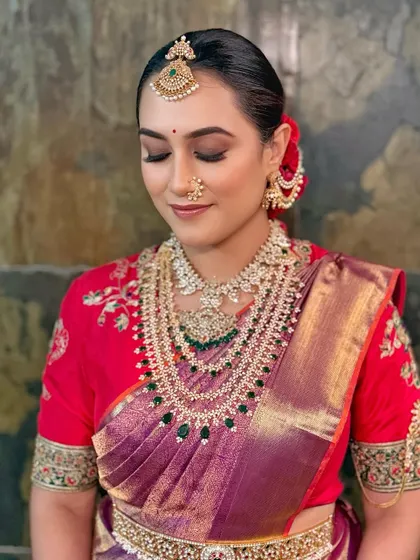 A divine look with kohl-rimmed eyes, dewy skin, and a traditional sleek bun adorned with red flowers.