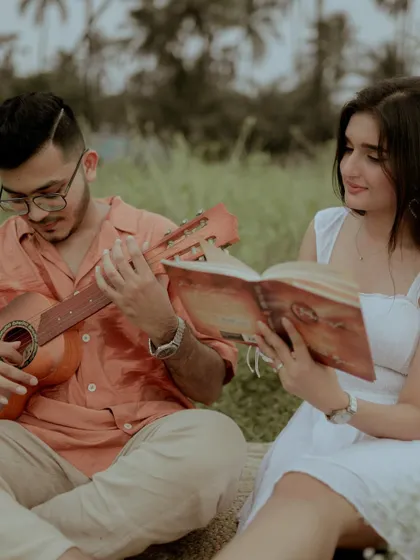 A candid moment of the couple enjoying their picnic, with him playing the guitar and her reading a book.