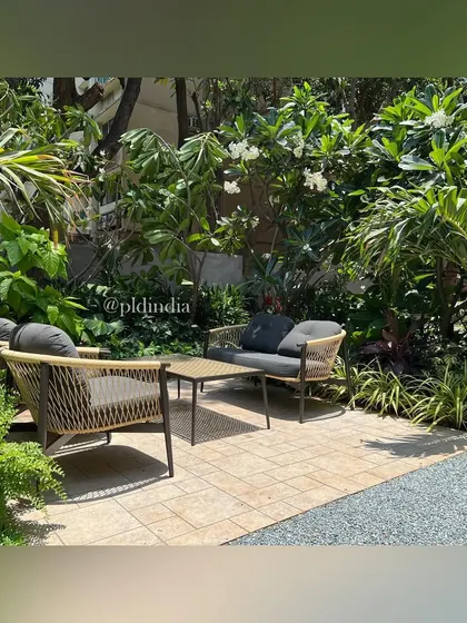 A close-up of the intimate seating area, framed by flowering Frangipani trees and lush palms. This composition highlights the creation of a private, resort-like feel within a residential entrance space.