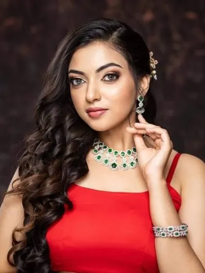 A western-style look from a photoshoot. The model is wearing a beautiful AD stone set with green stones that adds a touch of glamour to her red dress.