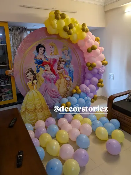 A magical Disney Princess themed backdrop for a birthday celebration. The large circular banner features iconic princesses and is framed by a pastel balloon garland, creating a fairy-tale setting.
