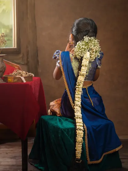 A girl in a traditional blue and gold lehenga, her hair beautifully braided with jasmine flowers ('moggina jade'). A portrait of quiet grace.
