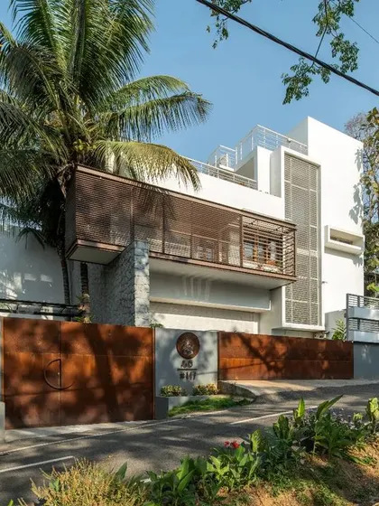 The front elevation of the Siri residence, a tropical contemporary home. The facade is layered with stone, white walls, and louvered screens that provide both shading from the western sun and privacy.