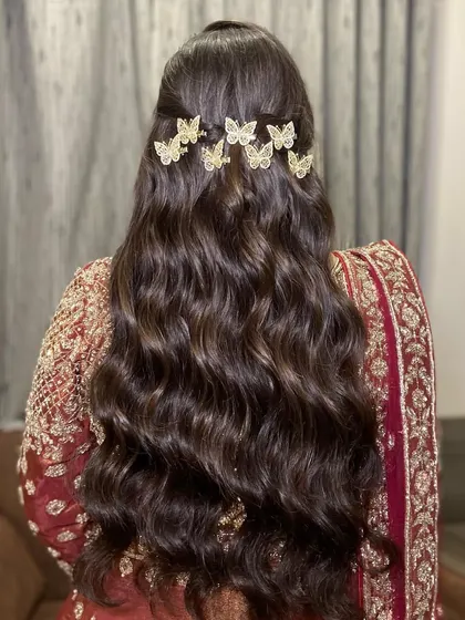 A beautiful hairstyle for a sangeet night. These soft waves are decorated with delicate butterfly clips, adding a romantic touch to her maroon and gold outfit.