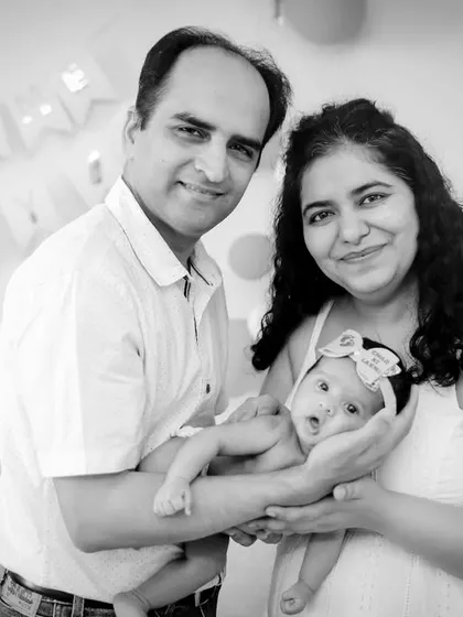 A beautiful first family portrait at home. The parents hold their newborn, smiling for a classic black and white photograph.