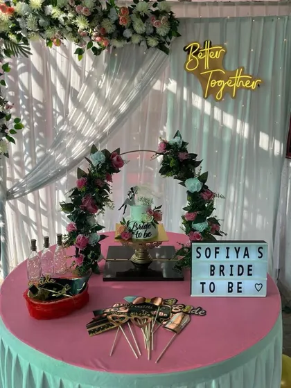 A complete bridal shower setup featuring a cake table, fun props, and a personalized light-box sign. The backdrop includes a floral arch and a "Better Together" neon sign.