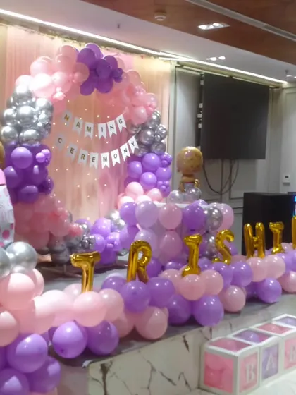 An angled view of the naming ceremony stage, highlighting the balloon pillars and the baby's name in large gold letters.