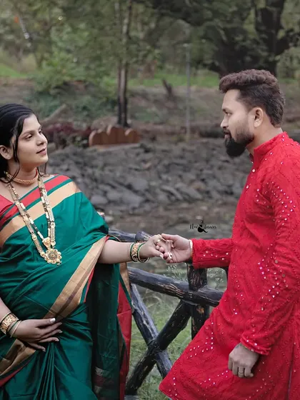 A moment of connection by the water. The contrast between her green saree and his red kurta is visually striking, highlighting their bond.
