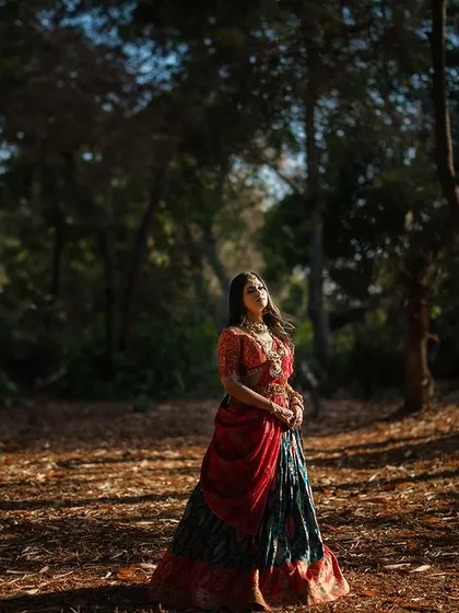 A wide shot of the bride in a forest clearing. The dappled sunlight on the ground and her solitary figure create a feeling of a fairytale moment.