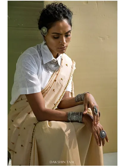 An editorial shoot with a unique styling concept, pairing a classic white shirt with a saree. The earthy tones and silver jewelry create a grounded, artistic look.