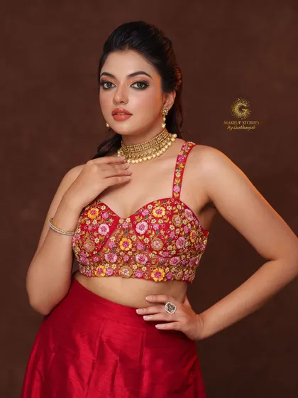 A modern lehenga look featuring a red bustier-style crop top with vibrant multi-color floral embroidery, paired with a simple red skirt.