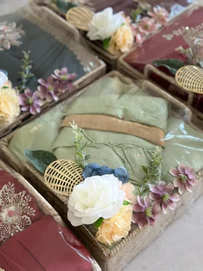 A pastel green outfit packed in a decorated jute basket. The soft color palette of the outfit and flowers creates a serene and elegant look.