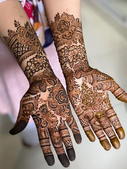 This floral henna design is wonderfully intricate, with different patterns on each hand for a unique touch. One hand features a large floral vine, while the other has a denser, more traditional layout.