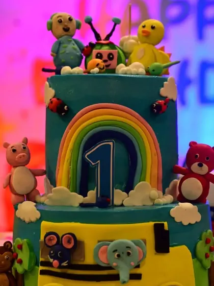 A fantastic two-tier Cocomelon cake, complete with edible figurines of all the characters, a rainbow, and the number '1'. I work with the best bakers to create themed cakes that taste as good as they look.