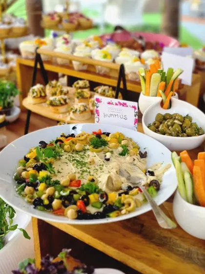 A beautifully presented bowl of hummus, garnished with chickpeas, olives, and fresh vegetables. This is a staple of our Mediterranean-inspired grazing tables, perfect for healthy and flavorful dipping.
