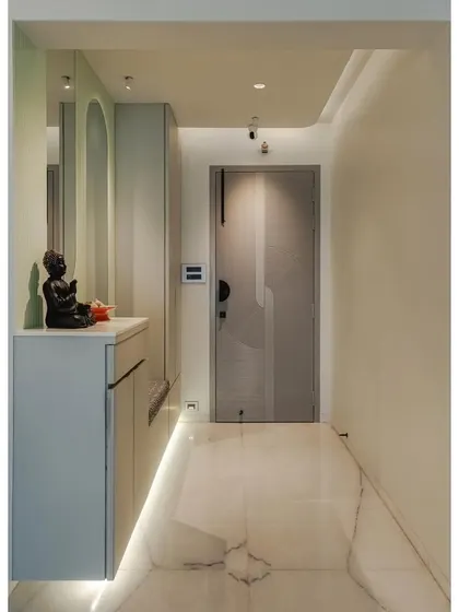 This view shows the complete entryway design, from the custom grey door to the floating console with a Buddha statue for a serene welcome. The cove lighting in the ceiling and along the floor adds a soft, ambient glow.