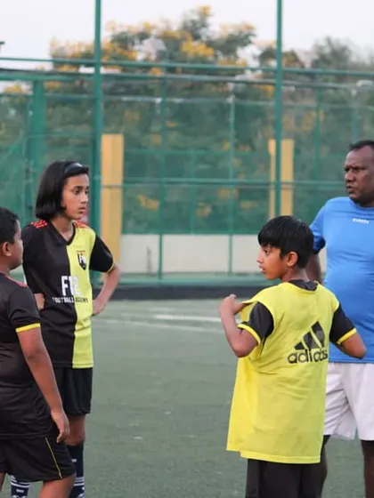 A coach leads a post-drill discussion with a group of young players, including boys and girls. We believe in breaking down the game and ensuring every child understands the strategy behind the skills.