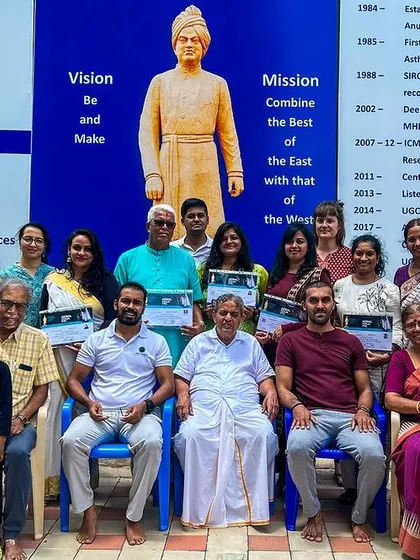 A group photo with students and faculty at the S-VYASA campus. The university's vision and mission, displayed behind us, guide our work in combining the best of the East and West.