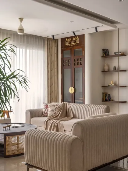 A wider view of the living room, showing the custom-designed pooja room door integrated into the space. The fluted sofa and soft furnishings create a cozy, inviting atmosphere.