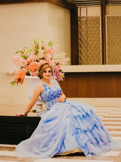 A solo portrait of the bride in a beautiful blue ball gown, seated gracefully in a luxurious hotel lobby. This shot highlights the elegance and grandeur of her engagement look.