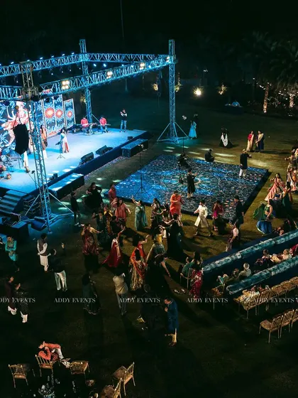 An aerial view of an outdoor stage and dance floor at night. The blue lighting on the stage truss and the patterned dance floor create a vibrant atmosphere for guests to enjoy live performances and dancing.